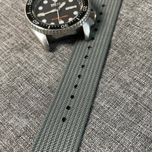 May include: A gray nylon watch strap with black stitching and a silver watch with a black face and silver hands. The watch face has the text "SEIKO DIVER'S 200m" printed on it.