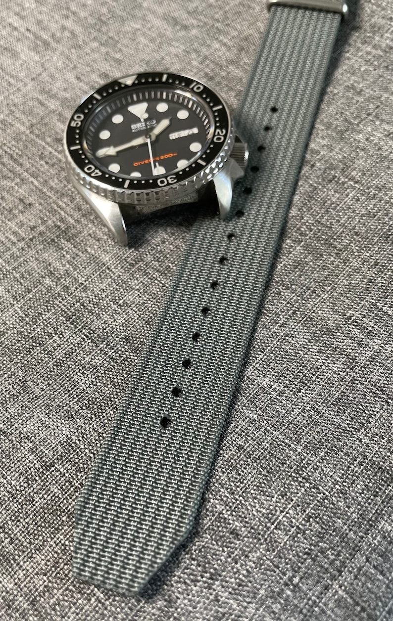May include: A gray nylon watch strap with black stitching and a silver watch with a black face and silver hands. The watch face has the text "SEIKO DIVER'S 200m" printed on it.