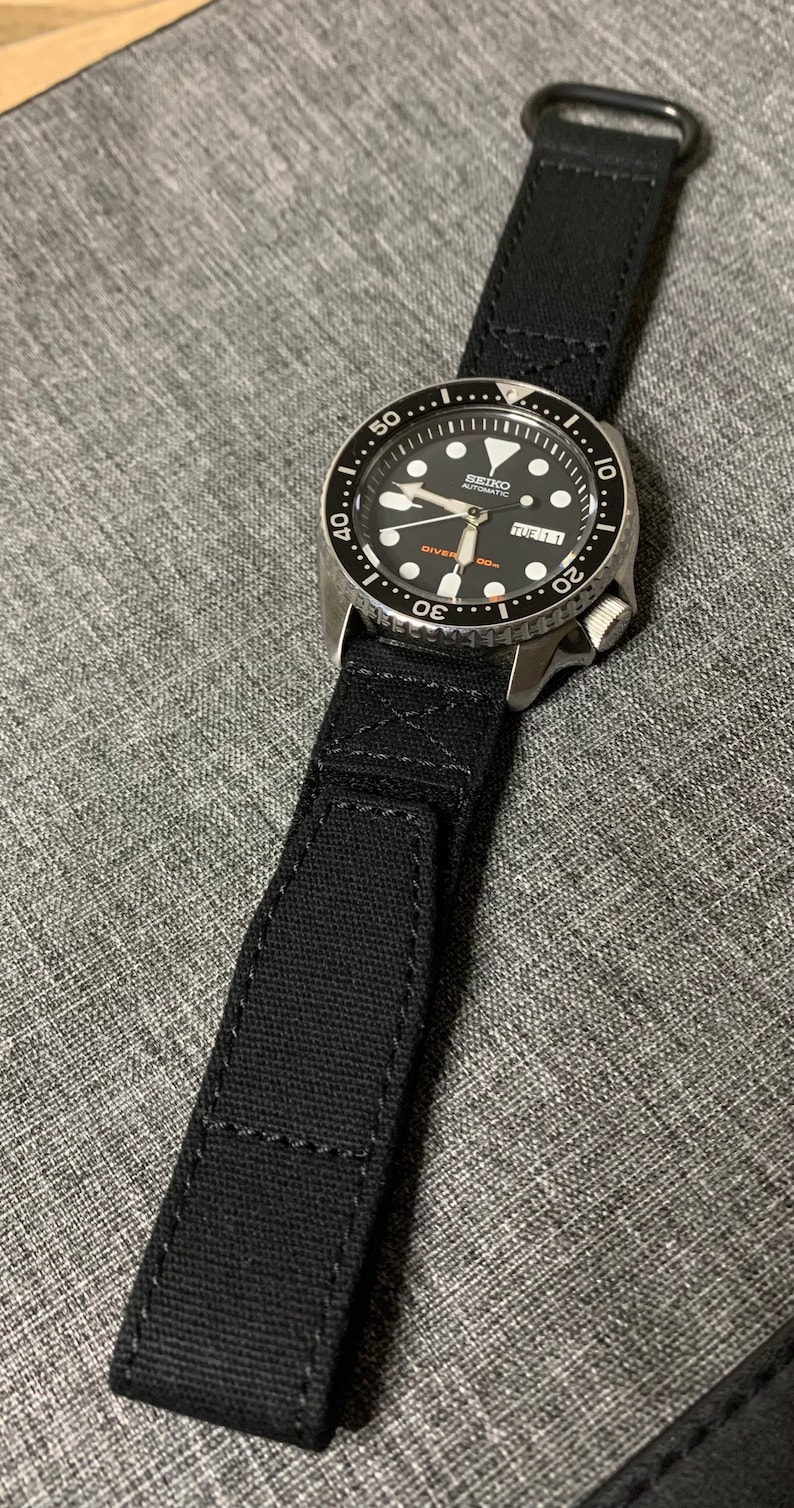 May include: A black Seiko automatic diver watch with a black canvas watch strap. The watch face has white markings and a date window.