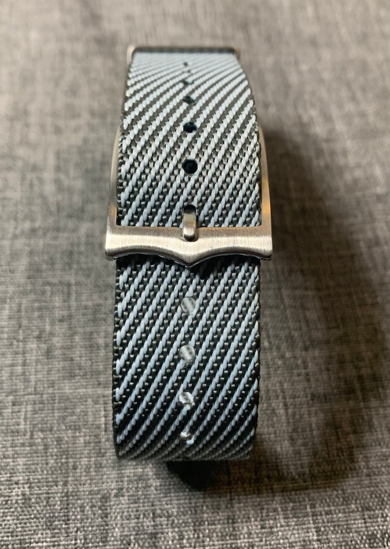 May include: A black and white striped watch strap with a silver buckle.