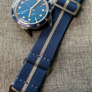 May include: A blue and white striped watch strap with a silver buckle. The strap is made of a woven fabric and has a subtle texture. The strap is designed to fit a wrist watch.