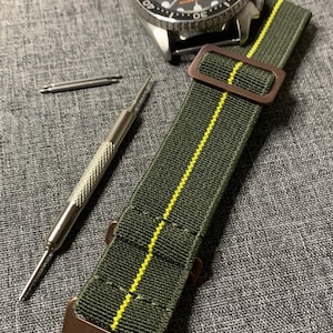 May include: A green and yellow striped nylon watch strap with a bronze buckle. The strap is designed for a watch with a 20mm lug width.