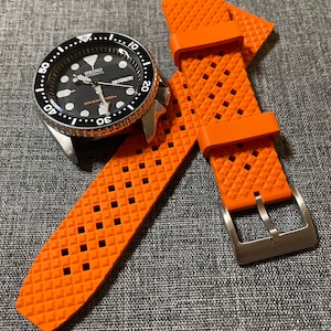Puede incluir: Correa de reloj de caucho naranja con un patr&oacute;n de diamante y una hebilla plateada. La correa est&aacute; dise&ntilde;ada para un reloj con una anchura de leng&uuml;eta de 20 mm.