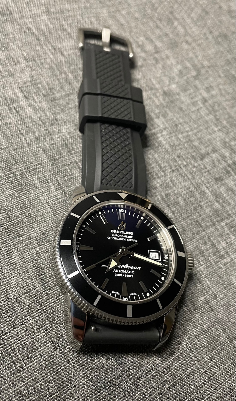 May include: A black Breitling Superocean Automatic 200m/660ft watch with a black rubber strap. The watch face has white markings and a date window.