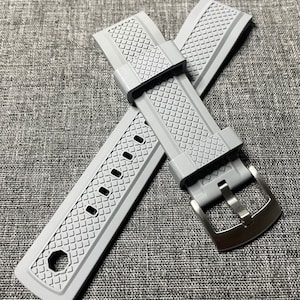 Puede incluir: Un par de correas de reloj de silicona gris con un patrón texturizado y una hebilla plateada.