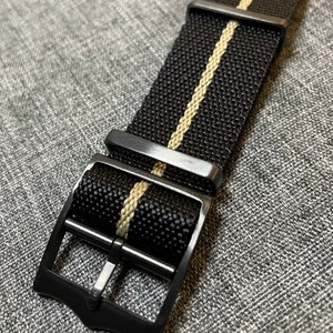 May include: Black watch strap with a single white stripe down the center. The strap has a black metal buckle.