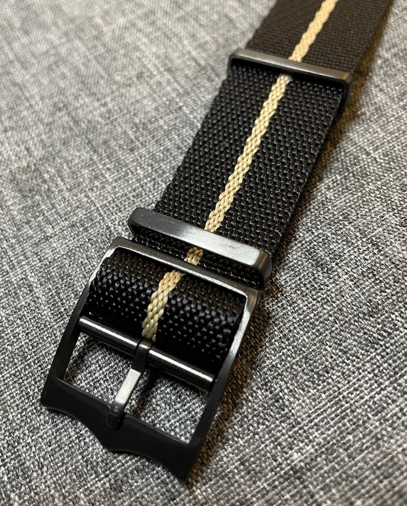 May include: Black watch strap with a single white stripe down the center. The strap has a black metal buckle.