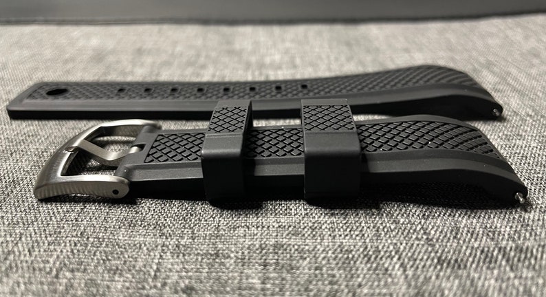 May include: A black rubber watch strap with a silver buckle. The strap has a textured pattern and is designed for a watch with a 22mm lug width.