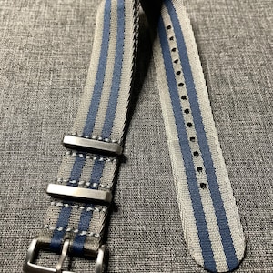 Op de afbeelding: Een grijs en blauw gestreept nylon horlogebandje met een zilveren gesp.