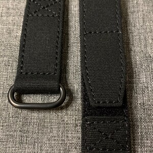 May include: Two black watch straps with a metal loop on one strap. The straps are made of a woven fabric with stitching around the edges.