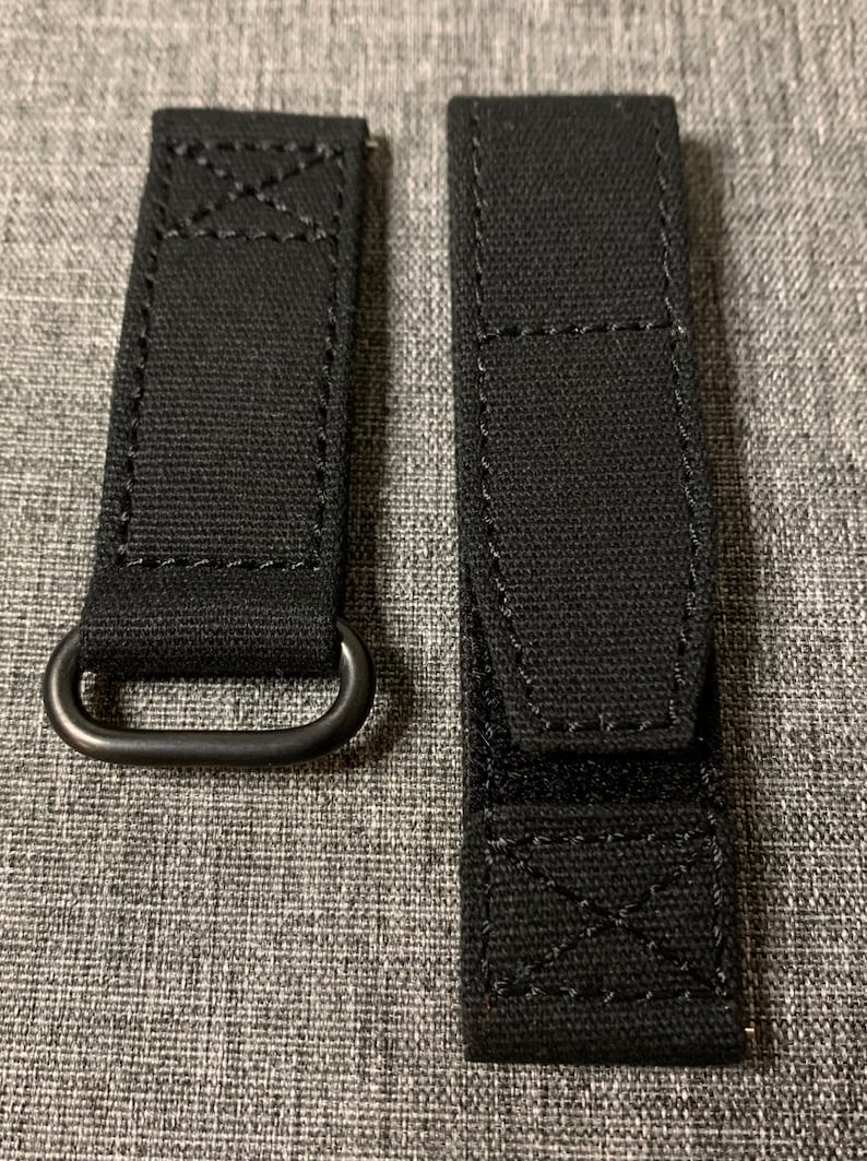 May include: Two black watch straps with a metal loop on one strap. The straps are made of a woven fabric with stitching around the edges.