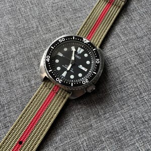 May include: A black Seiko watch with a green and red striped nylon watch band. The watch face has white markings and the text "SEIKO AUTOMATIC DIVER'S 200m".