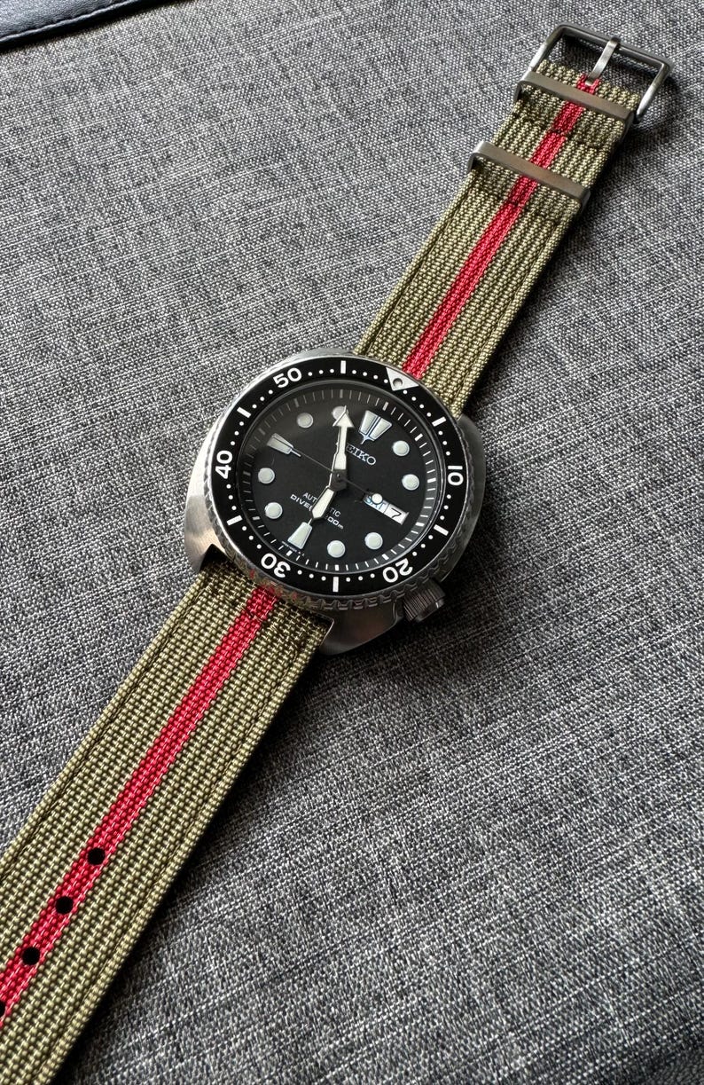 May include: A black Seiko watch with a green and red striped nylon watch band. The watch face has white markings and the text "SEIKO AUTOMATIC DIVER'S 200m".
