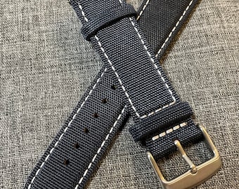 May include: A black watch strap with white stitching. The strap is made of a woven fabric and has a silver buckle.