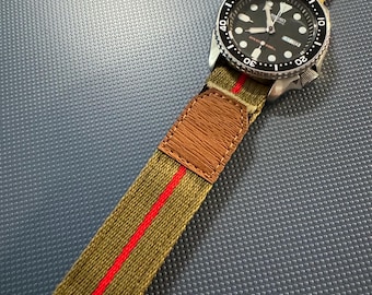 May include: A black and silver wristwatch with a black face and a green and red striped nylon watch band.