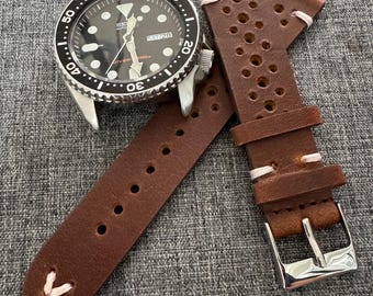 Puede incluir: Un reloj de pulsera negro y plateado con esfera negra y correa de cuero marrón. La correa del reloj tiene costuras blancas y una hebilla plateada. La esfera muestra el día y la fecha.