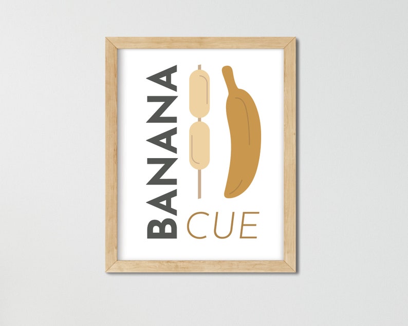 May include: A framed print with the text "BANANA CUE" in black and a graphic of a banana and a skewer with three small, round, beige items on it.