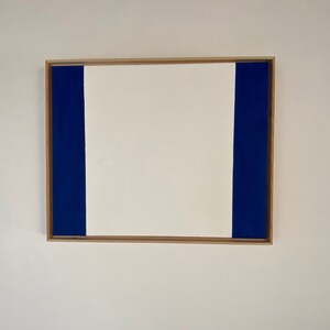 May include: A framed abstract painting with a white center and two blue vertical stripes on either side.