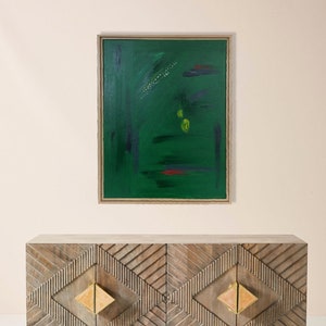 Puede incluir: Un armario de madera con tres cajones y patrones geométricos. Cada cajón tiene una manija de color dorado. El armario está frente a una pared con una pintura abstracta enmarcada con pinceladas verdes, azules y rojas.