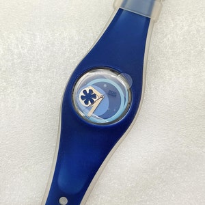 Puede incluir: Un reloj Swatch azul con una esfera blanca y un diseño azul y blanco. El reloj tiene una correa de silicona azul.