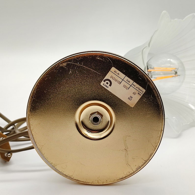 Może przedstawiać: Złota metalowa podstawa do lampy stołowej o okrągłym kształcie i śrubą w środku. Podstawa ma etykietę z tekstem "Art.-Nr. 0424810d, Code 1012l, max. 60 Watt, 230 Volt".