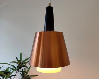 May include: A mid-century modern pendant light fixture. The light has a copper-colored conical shade, a black cylindrical top, and a white cord. The light is suspended from the ceiling, with a soft glow emanating from the bottom.