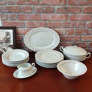 Könnte beinhalten: Ein Set aus weißem Porzellan-Geschirr mit einem zarten Blumenmuster. Das Set beinhaltet eine große ovale Platte, eine Suppenterrine mit Deckel, eine Sauciere und mehrere Speiseteller und Salatteller.