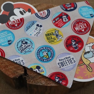 May include: A triangular bandana with a light gray background and a repeating pattern of colorful circular patches featuring various Disney characters, including Mickey Mouse, Minnie Mouse, Donald Duck, and Goofy. The patches have white outlines and feature text such as "Mickey", "Minnie", "Donald Duck", and "Sweeties".