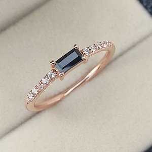 May include: A rose gold ring with a black rectangular gemstone and a band of small clear gemstones.