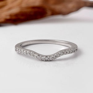 May include: A delicate silver band with a curved design and a row of small, clear diamonds.