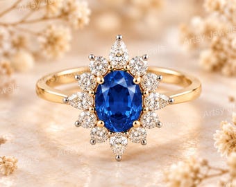Può includere: Un anello in oro con una pietra blu centrale dal taglio ovale circondata da un alone di piccole pietre chiare rotonde e a forma di pera. La fascia è in oro lucido e l'incastonatura presenta una disposizione a raggiera.