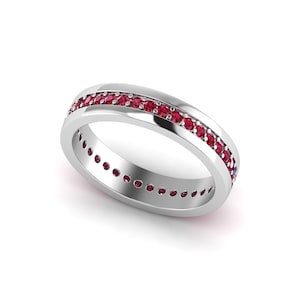 Peut inclure: Une bague en argent avec une rangée de petites pierres précieuses rouges rondes sur les bords supérieur et inférieur. La bague est présentée sur fond blanc, mettant en valeur les pierres et le métal poli.