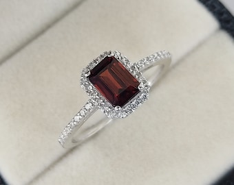 May include: A silver ring with a red gemstone surrounded by a halo of smaller white gemstones.