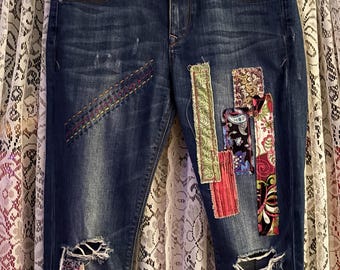 May include: Blue denim jeans with distressed details and colorful fabric patches sewn on. The waistband has a floral print and the label reads "Express Jeans".