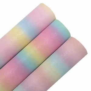以下が含まれることがあります： パステルカラーのキラキラしたクラフト素材の3つのロール。色は黄色から青、ピンクへと変化し、輝く仕上がりです。ロールはしっかりと巻かれており、様々なクラフトプロジェクトに適した、柔軟な紙のような素材でできているようです。