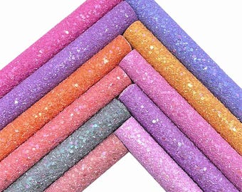 May include: A set of ten glitter fabric sheets in various shades of pink, purple, orange, and gray. The sheets are arranged in a fan shape, with the colors transitioning from light to dark.
