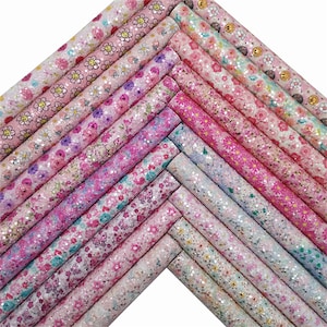 Op de afbeelding: Een verzameling van 18 roze en witte glitterstofbladen met verschillende bloemenpatronen, waaronder madeliefjes, vlinders en harten.