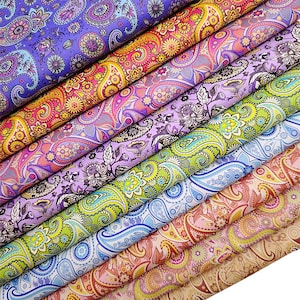 May include: A selection of paisley fabric samples in various colours. The fabrics display detailed floral and teardrop patterns in shades of purple, orange, pink, green, blue, and brown. The samples are arranged diagonally, highlighting the diverse designs.