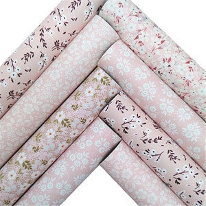 May include: Several rolls of floral patterned fabric in shades of pink. The fabric features white and brown floral and leaf patterns. The rolls are arranged diagonally, displaying the variety of designs. Ideal for craft projects.