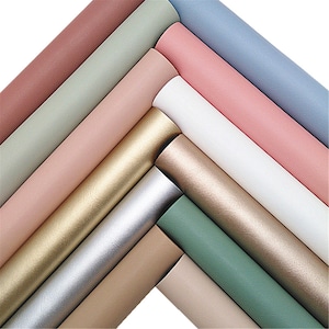 Pode incluir: Uma variedade de papel enrolado em várias cores pastel, incluindo rosa, azul, verde e dourado. Os rolos estão dispostos em um padrão diagonal, mostrando os diferentes tons e texturas. O papel parece liso e possivelmente metálico.