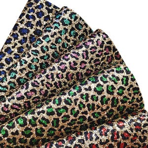 May include: Close-up of several sheets of fabric with a gold glitter leopard print. The leopard spots are in various colours, including blue, green, pink, and red. The fabric is folded over itself.