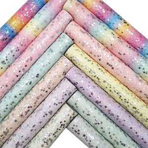 Peut inclure: Plusieurs feuilles de papier artisanal pailleté roulées, dans des tons pastel comme le rose, le jaune et le bleu. Chaque feuille est ornée de paillettes argentées en forme d'étoiles, créant un effet scintillant. Le papier est disposé en diagonale.