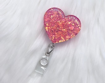 Könnte beinhalten: Rosa glitzernder Herzförmiger Badgehalter mit einem durchsichtigen Plastikband und einem silbernen Drehverschluss.