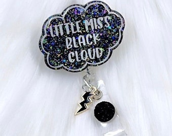 以下が含まれることがあります： 「Little Miss Black Cloud」という文字が書かれた黒いグリッターの雲の形をしたバッジホルダーと、黒いグリッターの稲妻のチャーム
