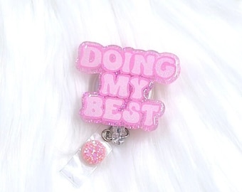 May include: Pink glitter badge reel with the text "DOING MY BEST" in white letters.