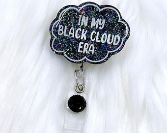 以下が含まれることがあります： 「In My Black Cloud Era」というテキストが書かれた、黒いグリッターの雲の形をしたバッジホルダーです。