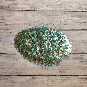 Puede incluir: Un mont&oacute;n de purpurina iridiscente de color verde azulado y dorado sobre un fondo de madera clara.