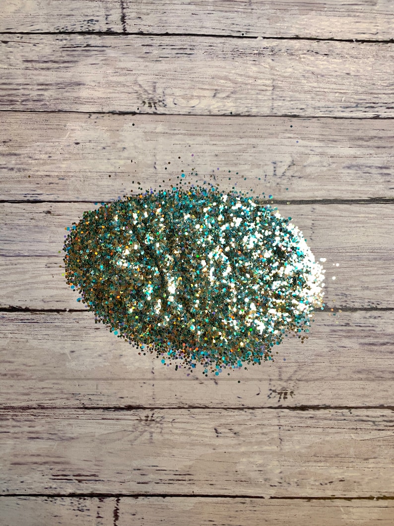 Puede incluir: Un mont&oacute;n de purpurina iridiscente de color verde azulado y dorado sobre un fondo de madera clara.