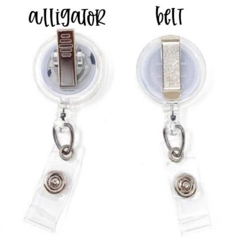 May include: Two clear plastic retractable badge holders with silver clips. The top holder has the word "alligator" printed on it. The bottom holder has the word "belt" printed on it.