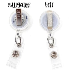 May include: Two clear plastic retractable badge reels with metal hardware. The left reel features an alligator clip labeled 'alligator' above it, and the right reel features a belt clip labeled 'belt' above it. Both have a clear vinyl strap.